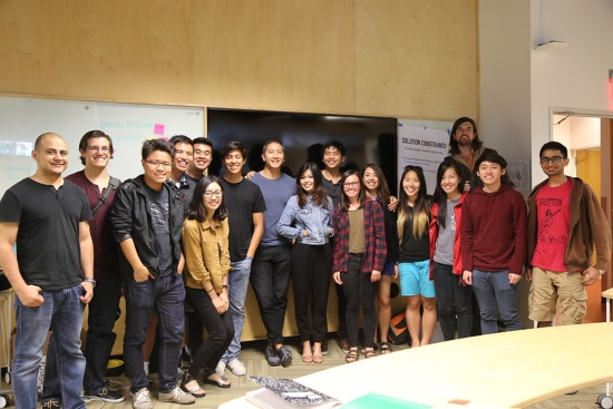 A group of undergraduate students stands together in a conference room, smiling for a picture.