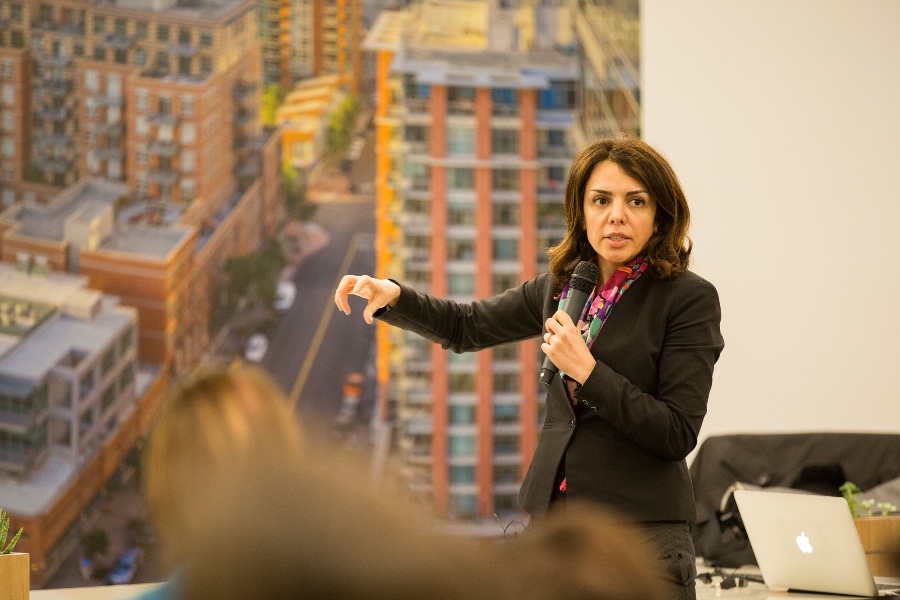 speaker gesturing in front of an image of a city