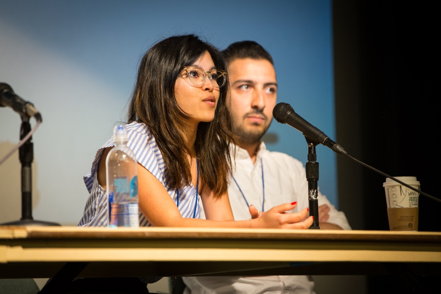 Two panel members at the Design at UC San Diego conference sit behind a table, one speaking into a microphone.